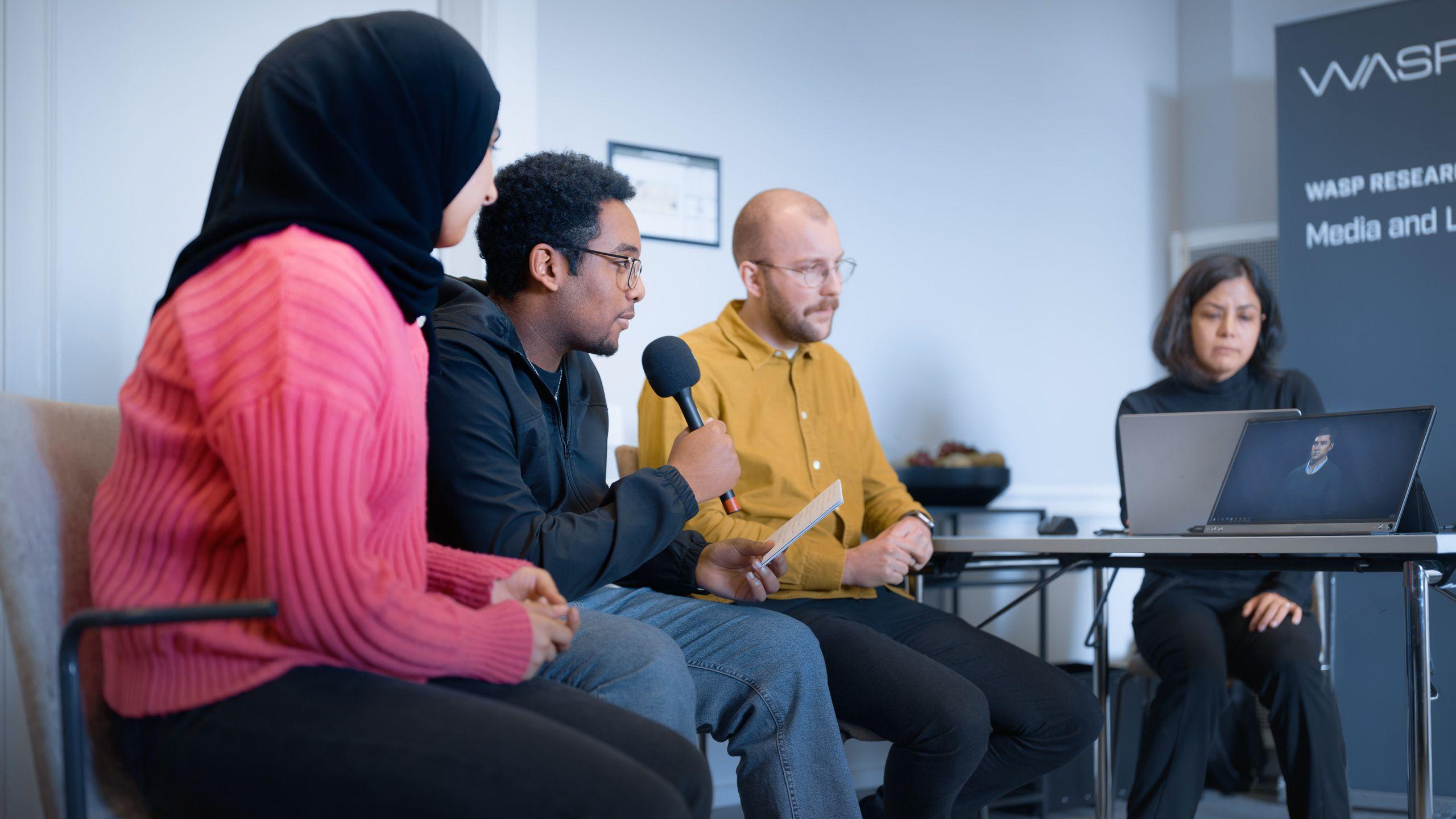 Två män och två kvinnor sitter och samtalar kring ett bord med en dator på